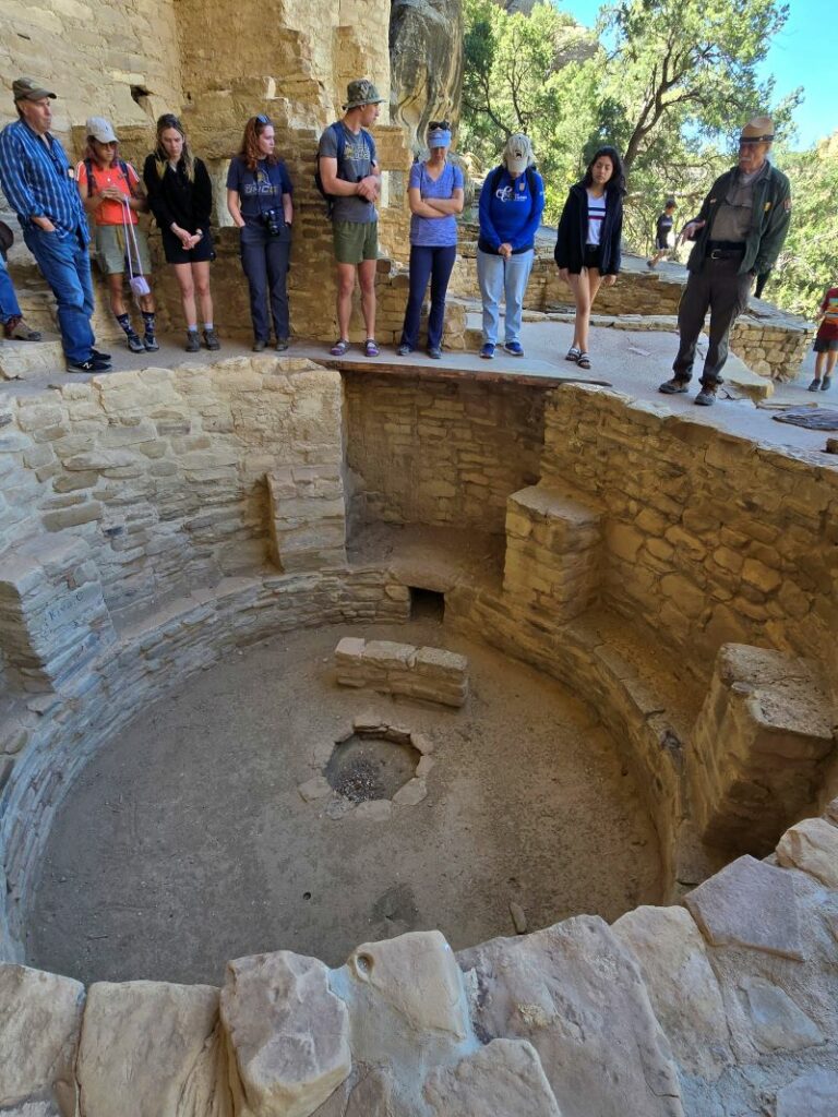 ranger standing next to kiva with fireplace at cliff palace